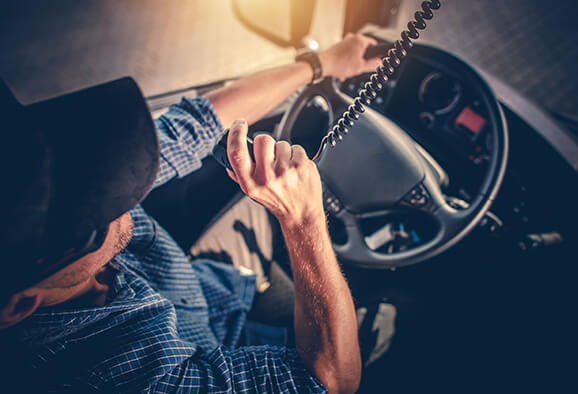 Over the top photo of a truck driver sitting behind the wheel of the a semi tractor using the CB radio